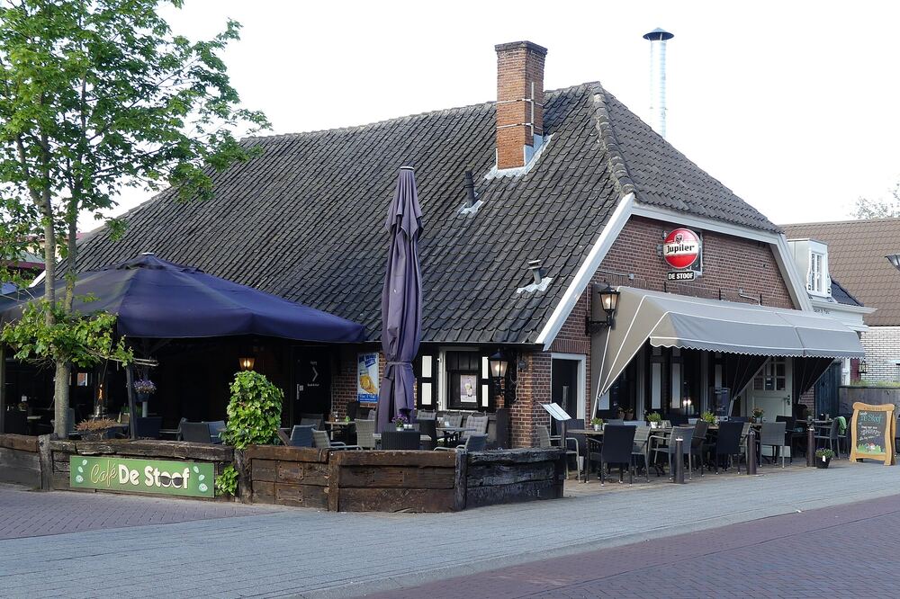 Eetcafe met donker terras, parasols en stoelen voor een pand met een puntdak aan een dorpsstraat